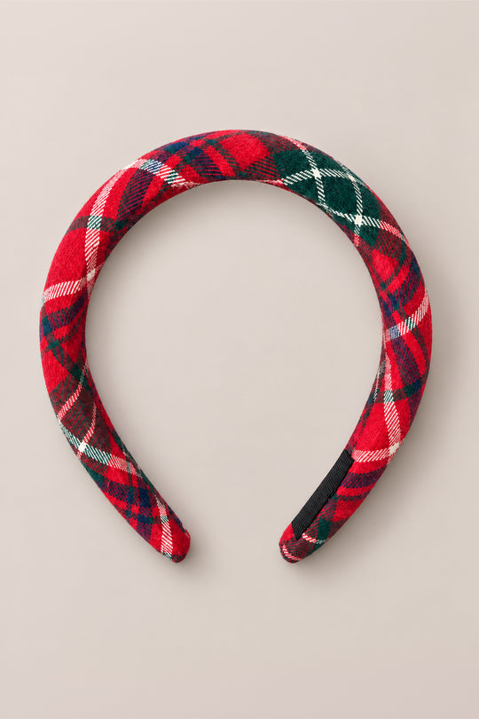 The Ivy City Co “Hair Bows in Christmas Cheer Plaid” headband, padded for comfort and covered in red, green, white, and navy plaid fabric, is displayed against a simple beige background—making it an ideal accessory for festive holiday photos.