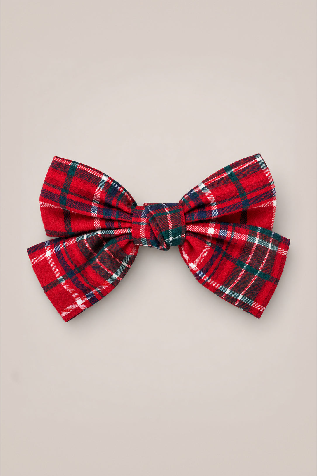The Hair Bows in Christmas Cheer Plaid by Ivy City Co—a festive red plaid accessory with green, white, and black stripes—makes the perfect holiday photo accent or Christmas bow, showcased elegantly against a plain beige background.