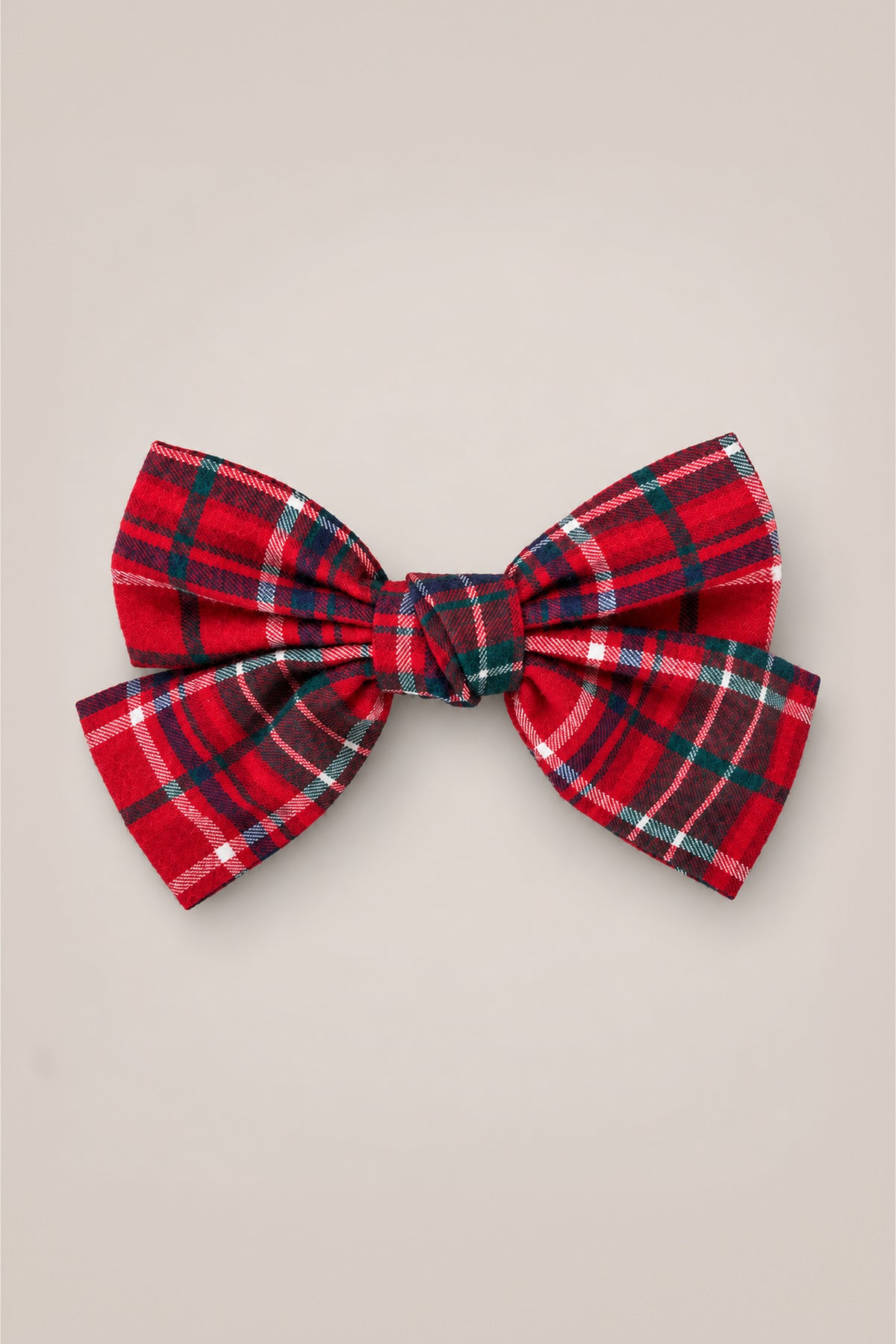 The Hair Bows in Christmas Cheer Plaid by Ivy City Co—a festive red plaid accessory with green, white, and black stripes—makes the perfect holiday photo accent or Christmas bow, showcased elegantly against a plain beige background.