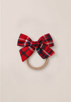 The Hair Bows in Christmas Cheer Plaid by Ivy City Co feature a red and navy plaid fabric bow attached to a hair tie, making them the perfect holiday photo accessory, shown here on a simple light background.