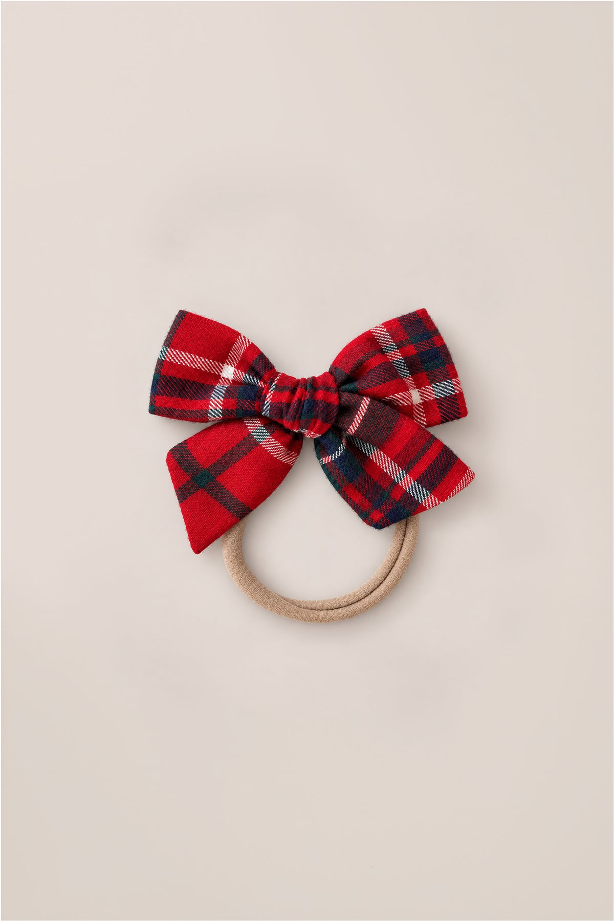 The Hair Bows in Christmas Cheer Plaid by Ivy City Co feature a red and navy plaid fabric bow attached to a hair tie, making them the perfect holiday photo accessory, shown here on a simple light background.