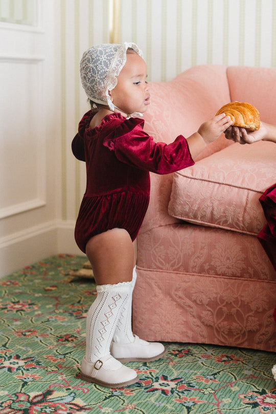 baby in a red velvet romper and white socks in a living room
