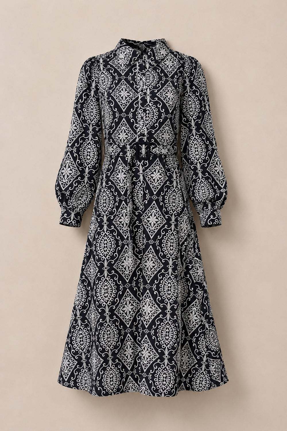 The Clover Dress in Midnight Tile by Ivy City Co features long sleeves, a midi length, and a high collar with intricate white geometric and floral patterns set against a deep, dark background. Displayed against a neutral backdrop, this nursing-friendly dress seamlessly blends elegance with practicality, making it ideal for any occasion.