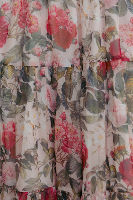 A close-up of the Cordelia Dress in Pink Bloom by Ivy City Co shows sheer, maternity-friendly chiffon with pink and red floral patterns and green leaves on a light background, arranged in horizontal tiers.