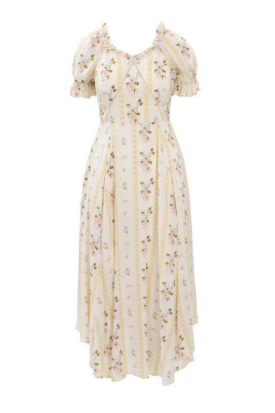 The Cottage Dress by Ivy City Co is a cream, midi-length dress with short puff sleeves, pink rose and green leaf botanical print, vertical yellow stripes, a fitted waist, and a ruffled sweetheart neckline.