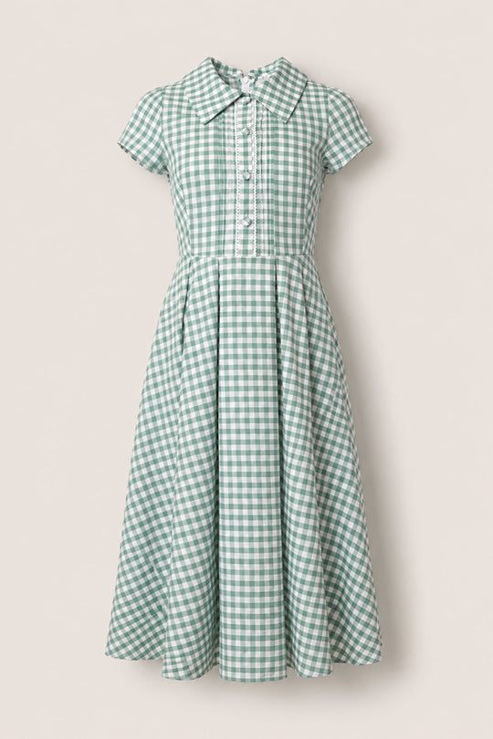 The Amber Dress in Sage Gingham by Ivy City Co features green and white checks on a cotton midi silhouette, complete with short sleeves, a fitted bodice, button-down front, and flared pleated skirt. Designed with a pointed collar and pleated detailing below the waist, this dress offers timeless charm.