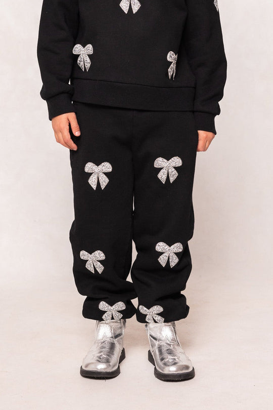 A child wearing Ivy City Co’s Mini Micah Jogger Sweatpants in Black, adorned with silver bows and paired with matching silver boots, stands against a plain background.
