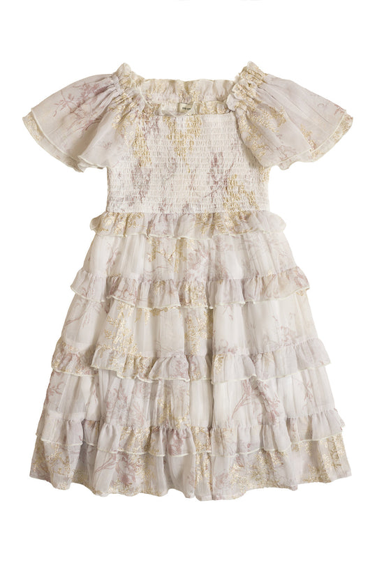 Introducing the Mini Winnie Dress in Bright White Wispy Wildflower by Ivy City Co—a delightful girls’ dress featuring short, gathered sleeves, a smocked bodice, and charming ruffled details. The dress is adorned with delicate gold and pink floral patterns and boasts a tiered, layered skirt, making it perfect for any special occasion.