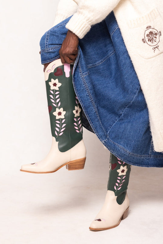 Person wearing floral-patterned green knee-high socks with white boots on a plain background