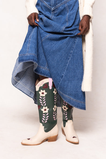 Person wearing a blue denim skirt, green floral boots, and white shoes on a white background