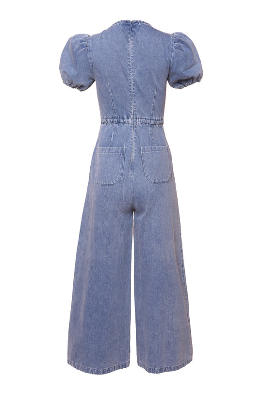 The Dallas Jumpsuit in Denim by Ivy City Co features a back view with short puff sleeves, fitted waist, two back pockets, wide-leg cropped pants, visible seams, and a zipper closure.