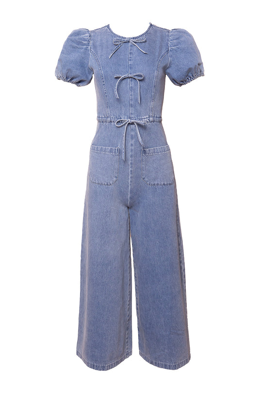 The Dallas Jumpsuit in Denim by Ivy City Co features short puff sleeves, a round neckline with two front ties, large front pockets, a drawstring waist, and wide-leg pants. The wide-leg jumpsuit is shown on a white background.