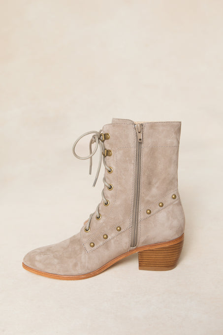The Darcy Lace Up Studded Boot by Ivy City Co features tan suede, a low wooden block heel, brass stud accents, and side zipper—displayed on a light beige background for chic style seekers.