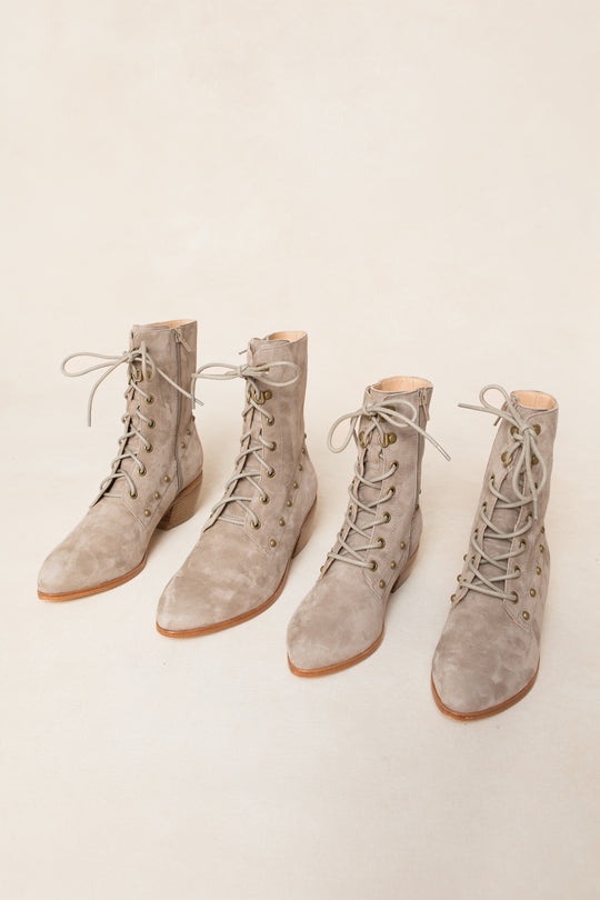Two pairs of Mini Darcy Lace Up Studded Boots by Ivy City Co, in light taupe suede with low wooden heels and pointed toes, are displayed side by side on a beige background—perfect for any stylish wardrobe.