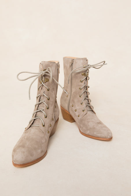 The Darcy Lace Up Studded Boot by Ivy City Co—a tan suede lace-up with side zippers, gold eyelets, and low stacked wooden heels—is displayed on a light background.
