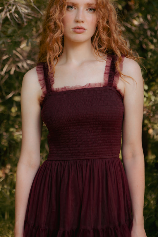 Woman wearing a burgundy dress with ruffled straps against a natural background