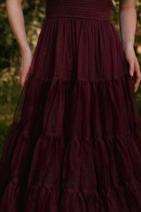 Maroon tiered dress with a blurred green background