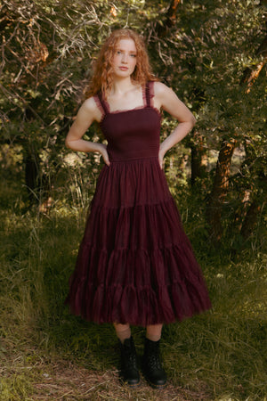 Woman wearing a burgundy dress with ruffled layers standing in a natural setting.