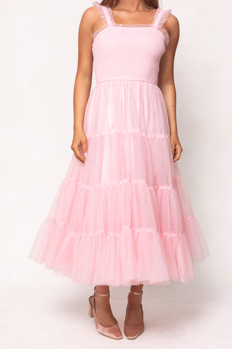 A person wears the Ivy City Co Destiny Dress in Pink, a sleeveless tulle dress with a smocked bodice and ruffled straps—maternity and nursing friendly—paired with pink pointed-toe heels, standing against a plain white background.