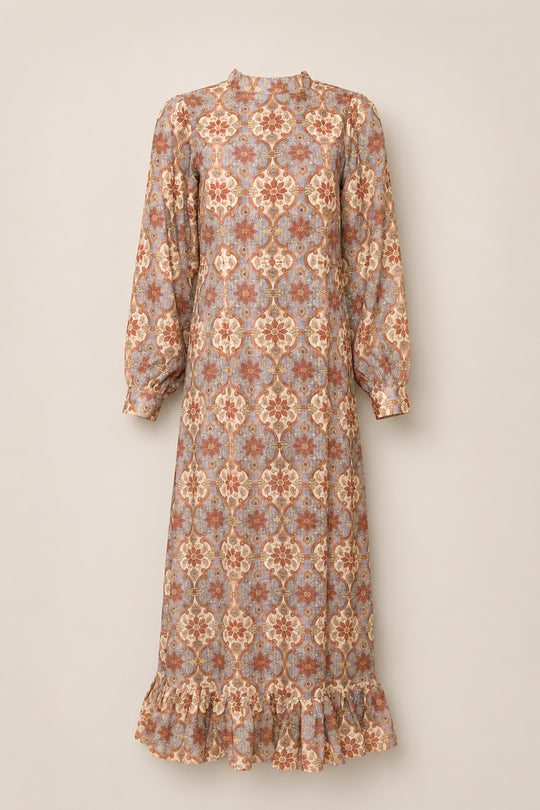 The Draper Dress in Golden Hour Tesserae by Ivy City Co is a long, vintage-inspired piece with a high neck, balloon sleeves, and a ruffled hem. Its fabric showcases an ornate floral and geometric pattern in muted shades of brown, cream, and dusty pink.