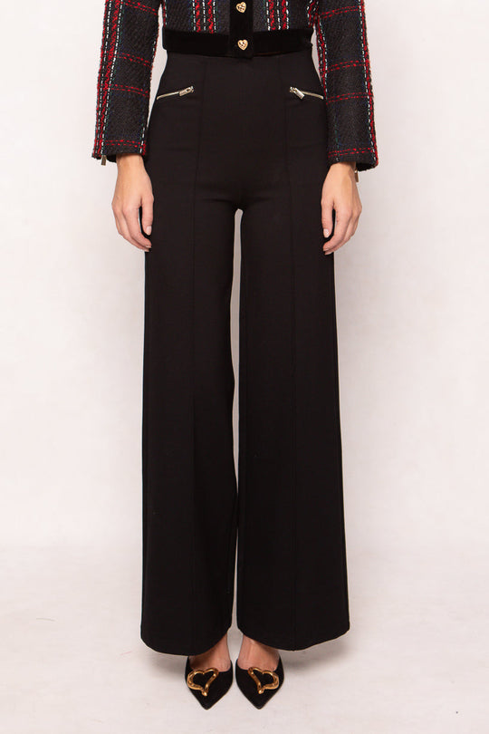 Wearing the Alyssa Pop Ponte Pants in Black by Ivy City Co—high-waisted wide-leg pants featuring front zipper pockets and subtle tummy control—styled with a textured black jacket adorned with red and green stripes, and finished with black pointed shoes featuring gold heart details for a chic day-to-night look.