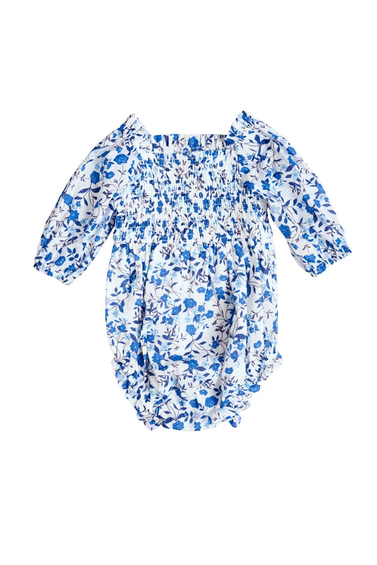 The Ivy City Co Baby Madeline Romper in Ditsy Cobalt Floral features a blue and white floral pattern, long sleeves with elasticized cuffs, and a smocked bodice, shown on a white background.