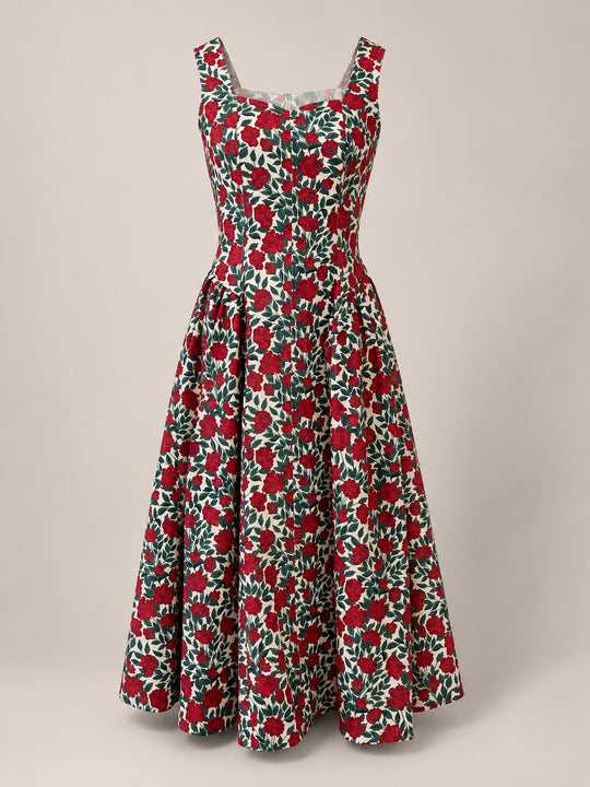 The Edith Dress in Red Roses by Ivy City Co is a sleeveless, vintage-inspired floral dress with a fitted bodice and flared skirt, showcasing a striking red and green rose pattern on a white background. The dress is presented against a neutral backdrop.