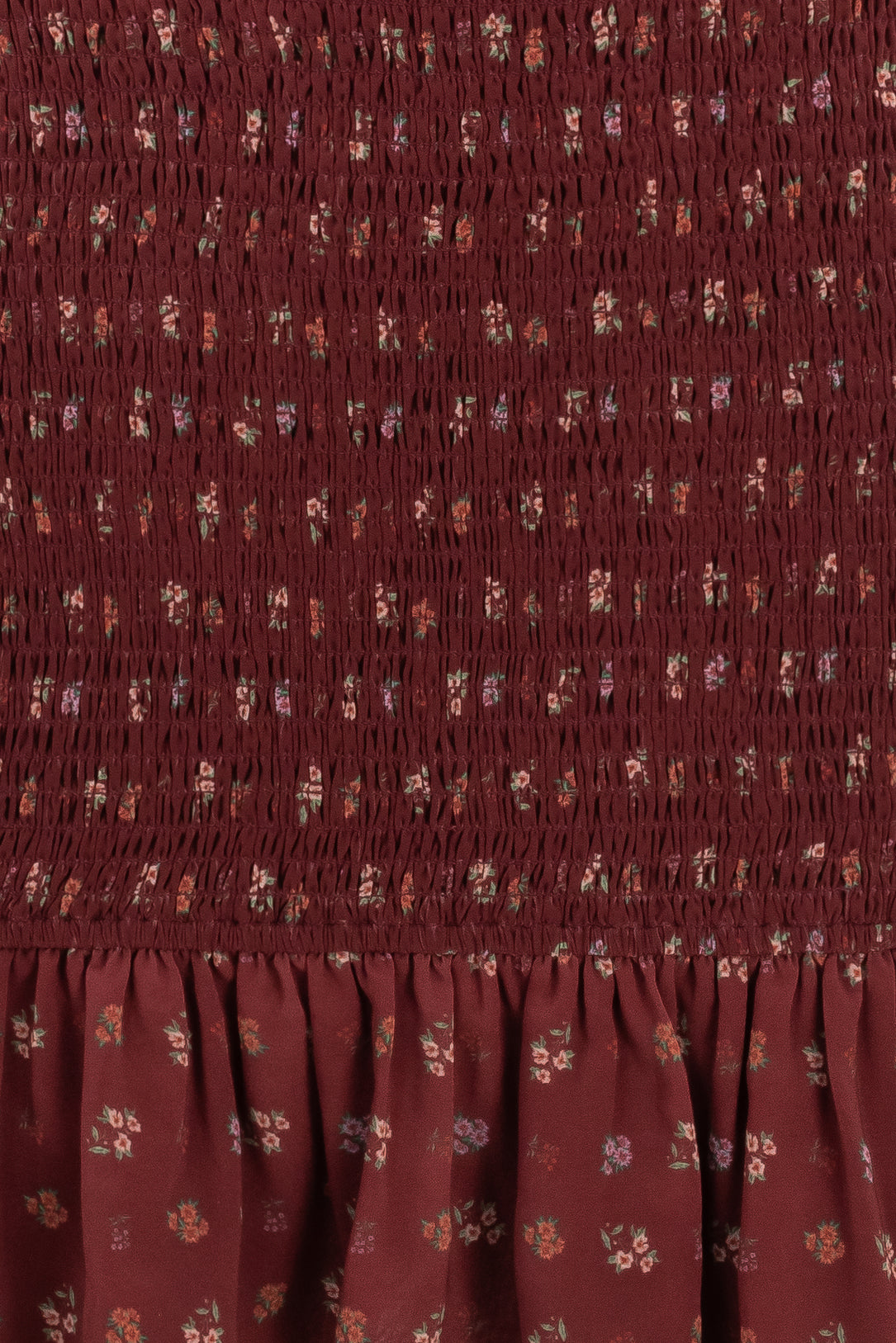 Close-up of the Elaine Dress in Mulberry Vine by Ivy City Co, featuring a maroon smocked bodice, ruched texture, ruffled hem, and scattered floral print in muted hues for added charm.
