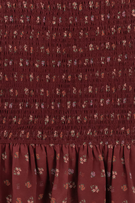 Close-up of the Elaine Dress in Mulberry Vine by Ivy City Co, featuring a maroon smocked bodice, ruched texture, ruffled hem, and scattered floral print in muted hues for added charm.