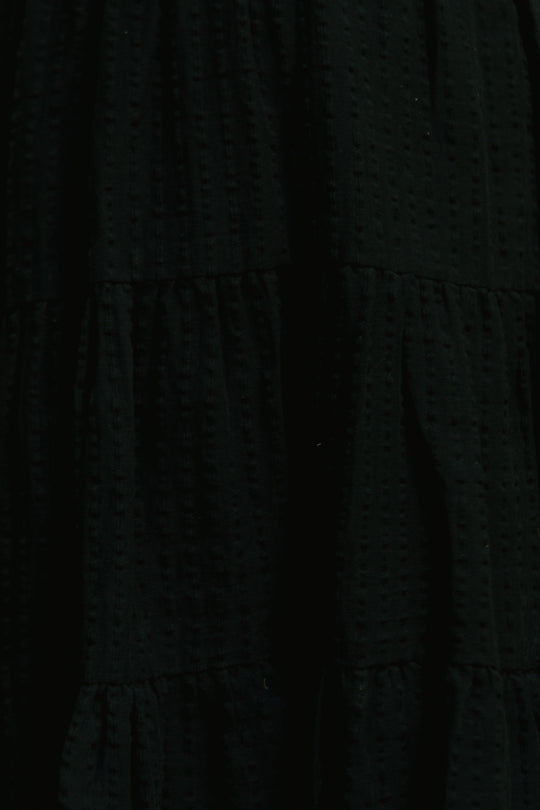 The Ellery Dress in Black by Ivy City Co features textured, dotted black cotton fabric with smocked, gathered tiered seams—maternity friendly and perfect as a chic black midi dress option.