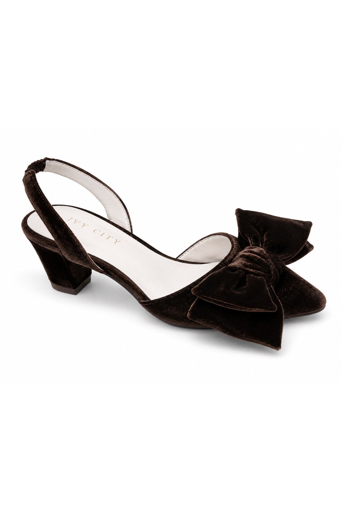 The Eloise Bow Heel in Brown by Ivy City Co features a low block heel, a stylish slingback design, and an oversized bow detail on the toe. Crafted with supple leather lining for all-day comfort, this elegant brown velvet shoe is displayed on a white background—twirl-ready and perfect to pair with your favorite dress.