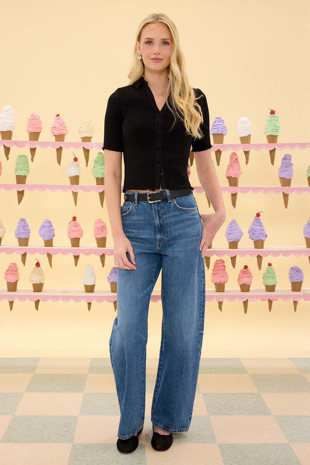 Woman wearing a black shirt and blue jeans standing in front of a colorful ice cream cone display.
