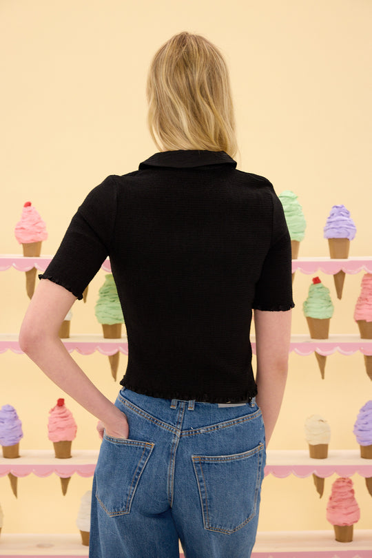 Person wearing a black shirt and blue jeans standing in front of a wall with ice cream cone decorations.