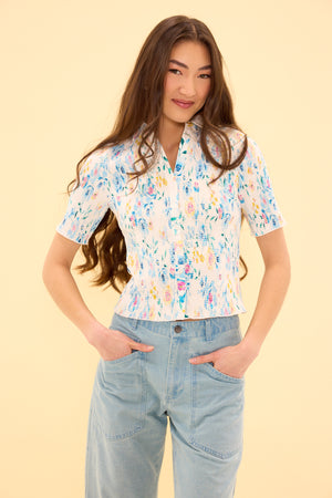 Woman wearing a floral blouse and jeans against a beige background