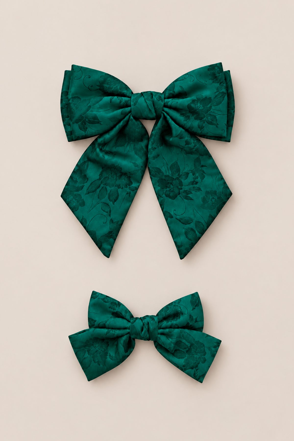 Two Hair Bows in Emerald Satin by Ivy City Co are displayed on a light beige background—one large and one small—arranged vertically with the larger bow above the smaller one. Their rich green floral pattern makes them perfect for use as an emerald hair bow or girls Christmas bow, and they are an ideal holiday photo accessory.