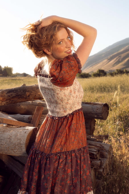 Woman in a historical dress standing in a field with mountains in the background