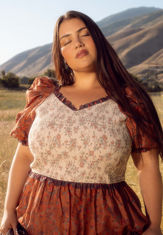 Woman in a floral dress standing in a field with mountains in the background