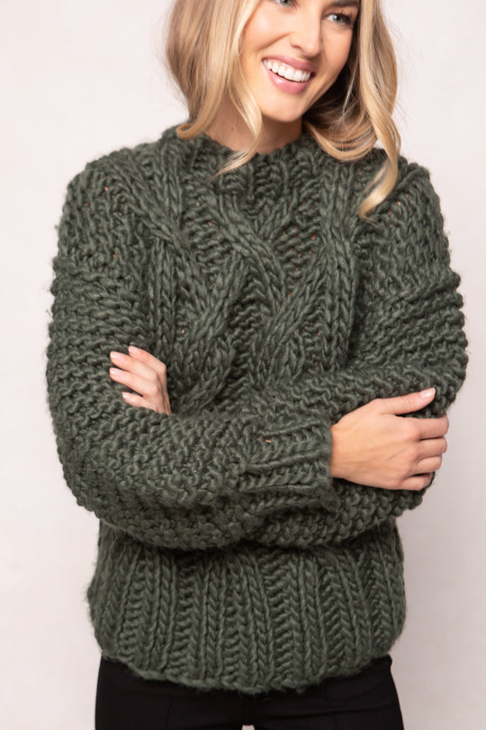 Woman wearing a green chunky knit sweater against a white background