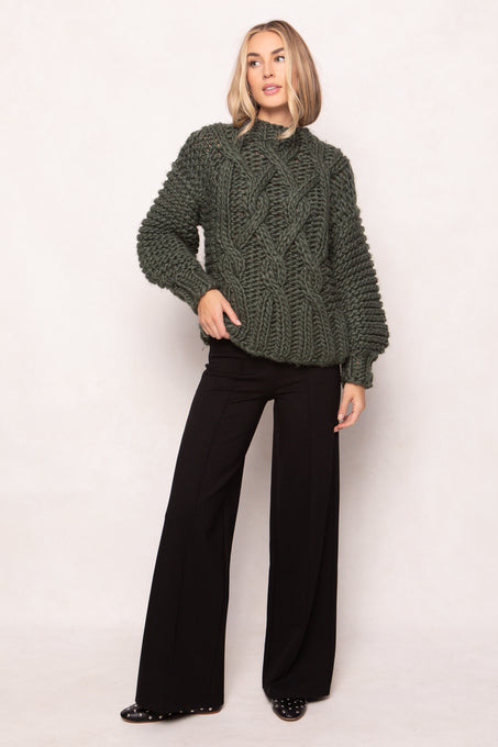 Woman wearing a green knitted sweater and black pants on a white background