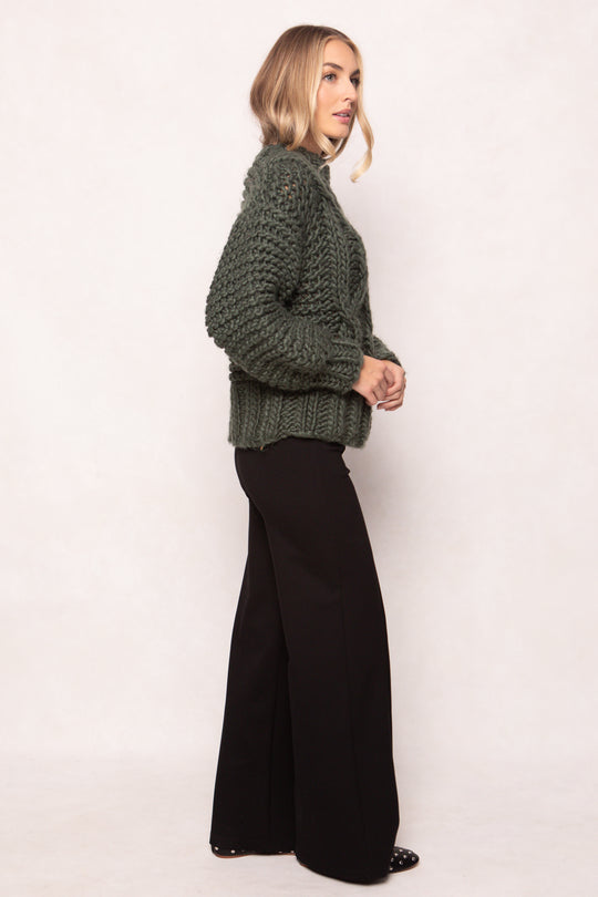 Woman wearing a green knitted sweater and black pants on a white background