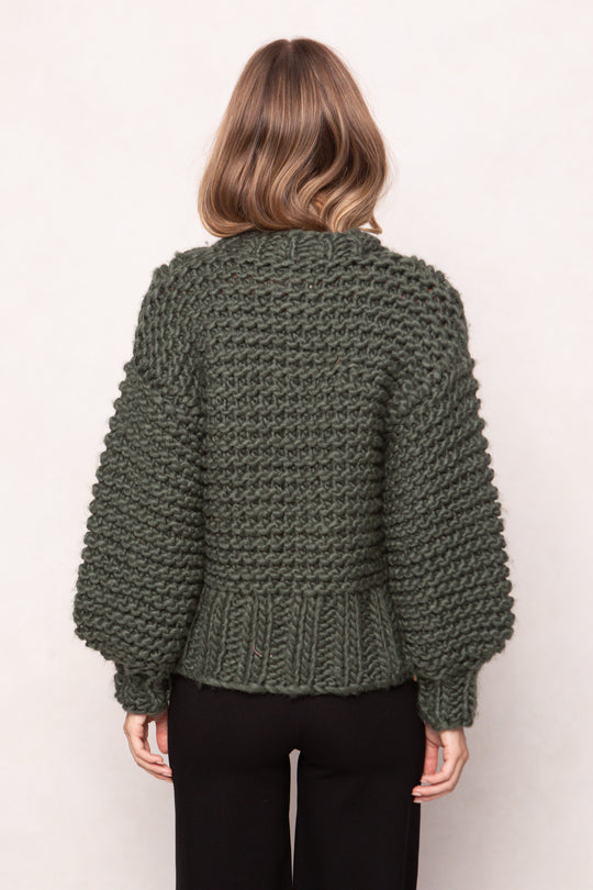 Person wearing a green chunky knit sweater on a plain background