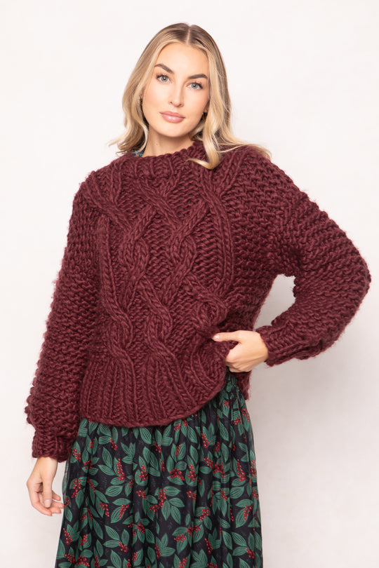 Woman wearing a chunky knit burgundy sweater against a white background