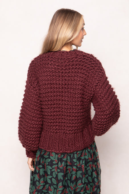 Person wearing a chunky knit burgundy sweater on a plain background