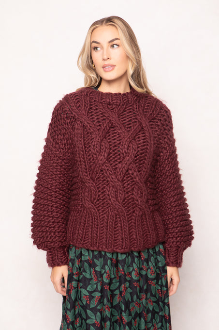 Woman wearing a chunky knit burgundy sweater with a plain background