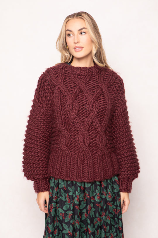 Woman wearing a chunky knit burgundy sweater with a plain background
