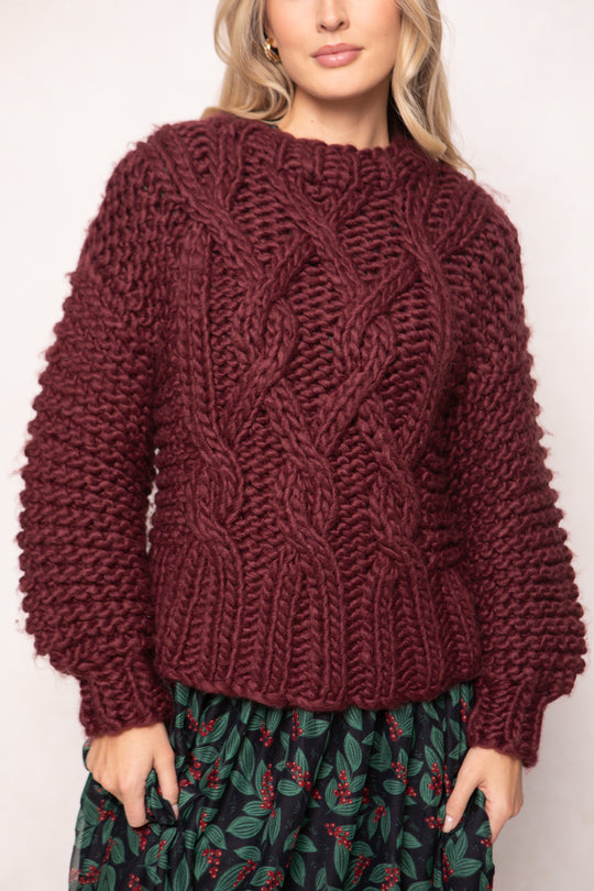 Person wearing a chunky knit burgundy sweater with a plain background