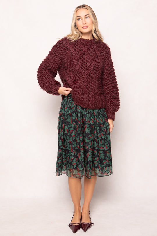 Woman wearing a maroon cable knit sweater and patterned skirt on a white background