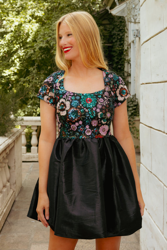 Woman wearing a floral top and black skirt standing outdoors.