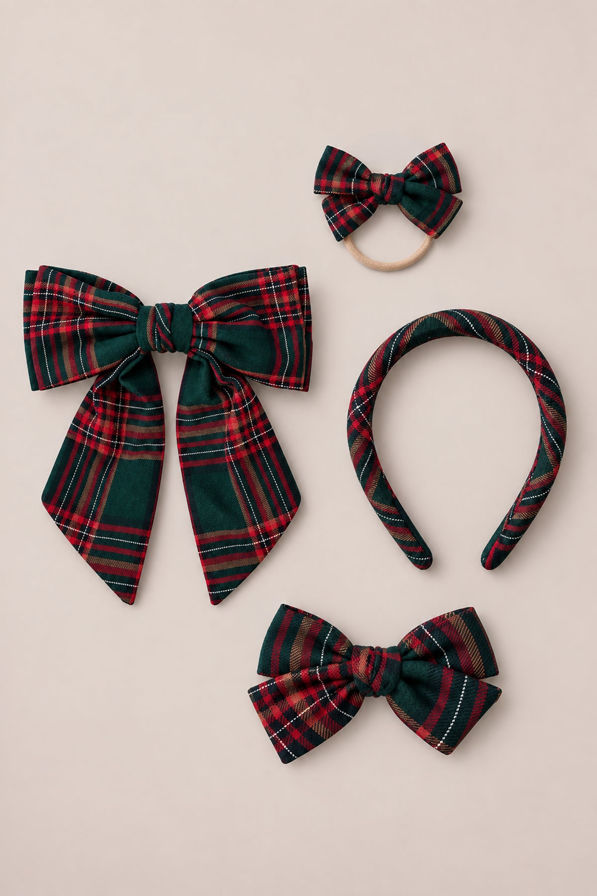 Four “Hair Bows in Evergreen Plaid” by Ivy City Co, crafted from cozy cotton flannel—featuring a large bow, a small bow on a hair tie, a holiday headband, and a medium bow clip—are all arranged on a beige background.