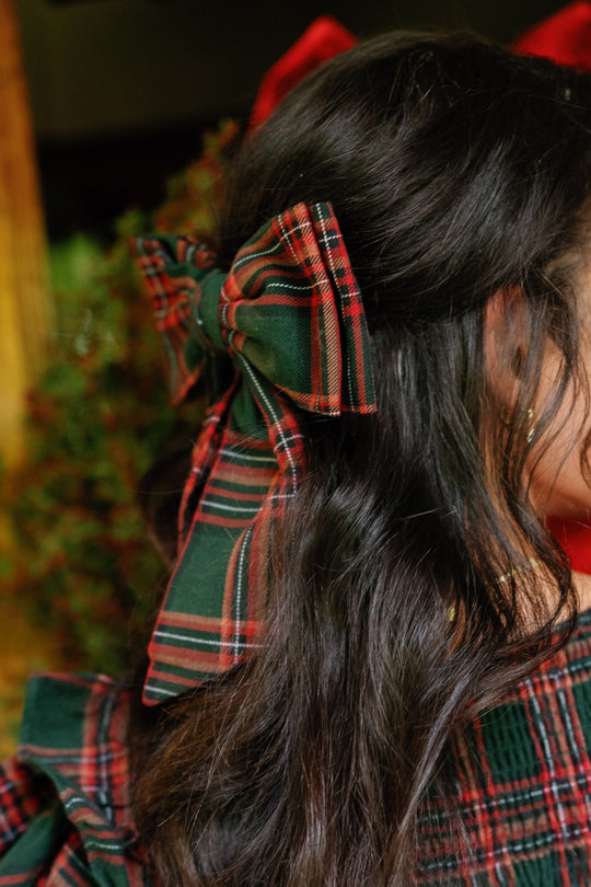 A person with wavy dark hair wears an Ivy City Co Hair Bow in Evergreen Plaid attached to the back of their head, perfectly matching their cotton flannel plaid outfit.